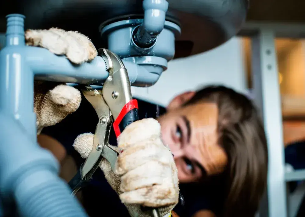 Plumber using pliers to repair a pipe connection beneath a sink
