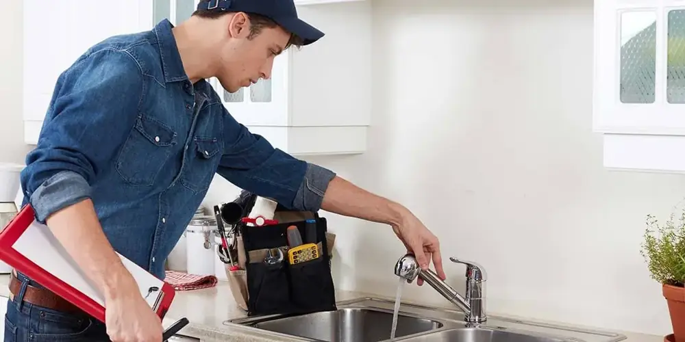 Plumber testing water flow at a kitchen faucet during a repair visit