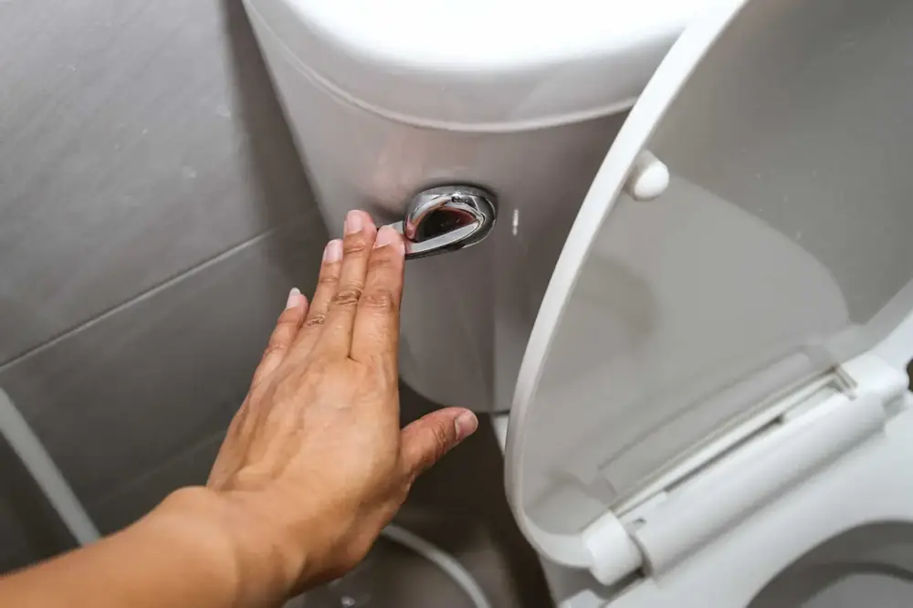 Close-up of a hand operating a toilet tank flush handle during a repair